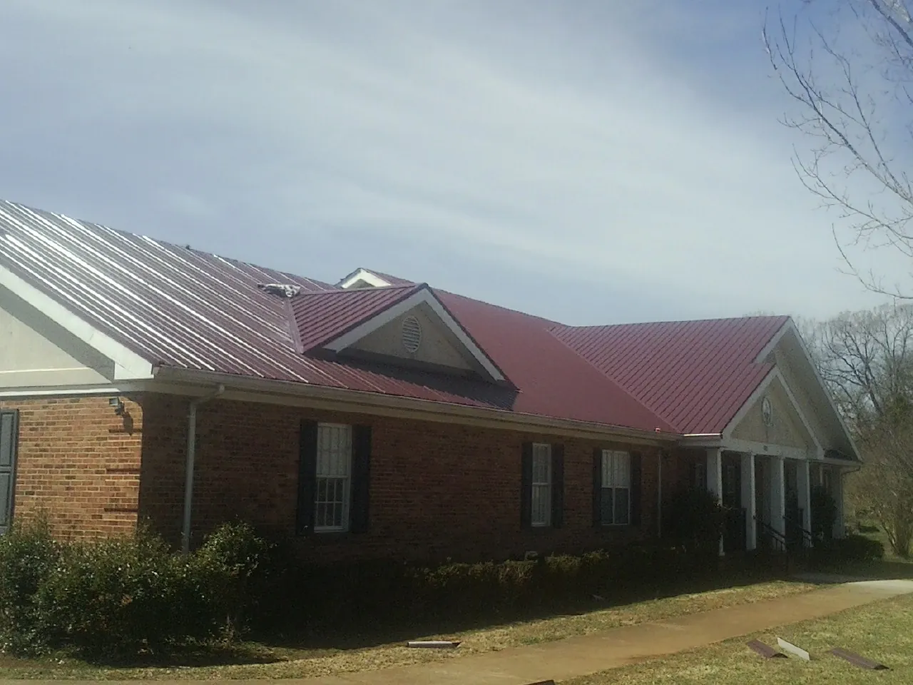 Red metal roof with gabled entries on a long brick building, from a Hail Damage Roof Repair job in Weippe