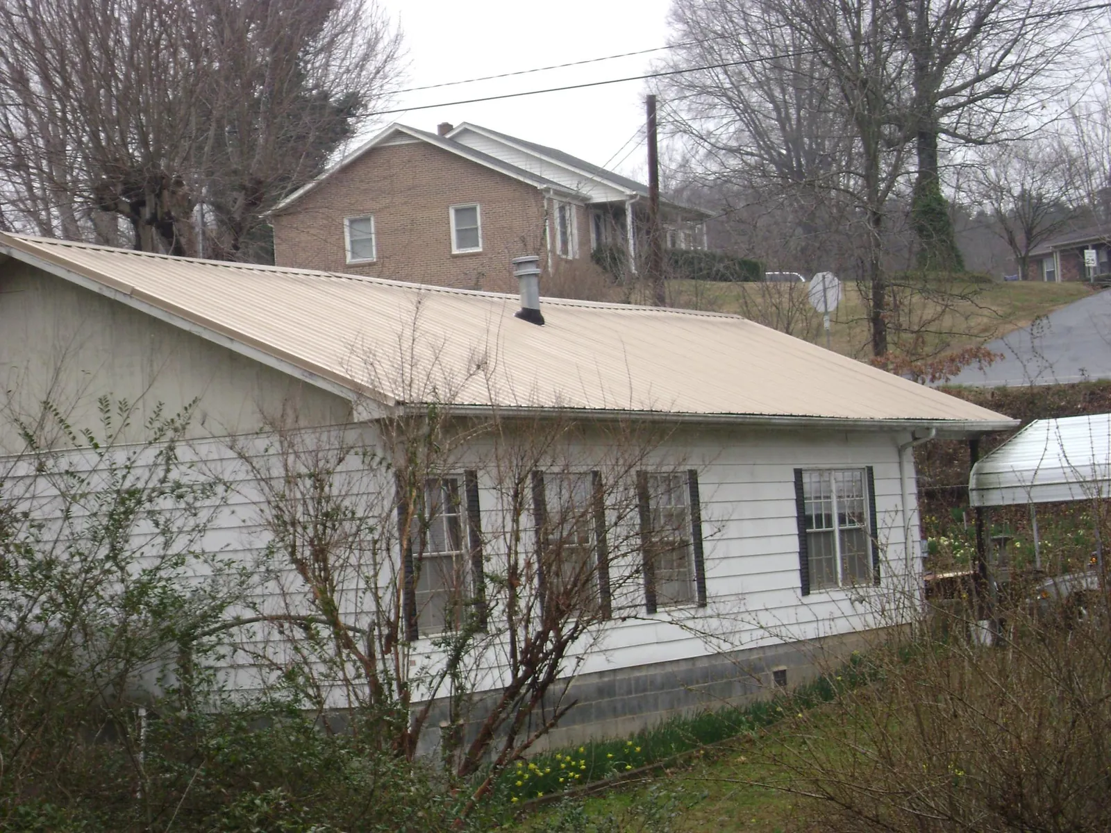 Tan metal roof on a white sided house set into a hillside — Commercial Roofing by Roofing Brothers in Weippe